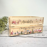 A personalized wooden Christmas Eve box with a natural pine finish, decorated with festive illustrations including Santa Claus, a reindeer, and a winter village scene. The front features the custom name 'Annabel's' in black script, and the bottom drawer is labeled 'Christmas Eve Box'.